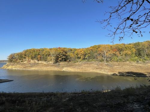 A serene landscape featuring a calm lake bordered by trees with autumn foliage under a clear blue sky.