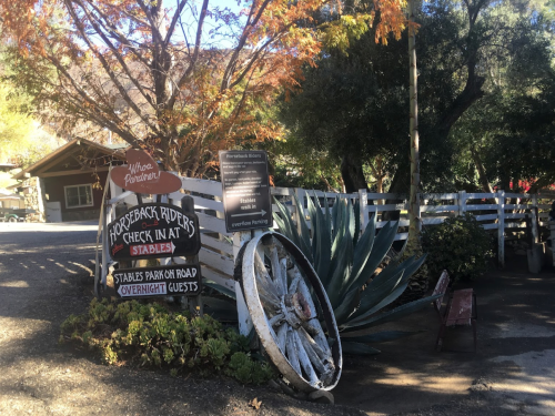 A rustic sign for horseback riding with a large wheel and colorful autumn foliage in the background.
