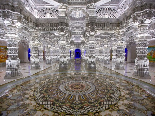 Intricate white marble temple interior with ornate pillars and a colorful patterned floor, illuminated by soft lighting.