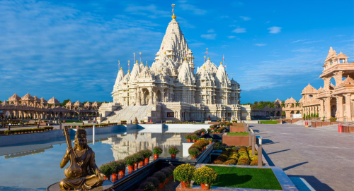 A grand temple with intricate architecture, surrounded by gardens and a reflective pool under a clear blue sky.