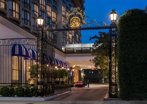 Elegant entrance gate of a hotel at dusk, featuring decorative ironwork and purple awnings, with a car parked nearby.