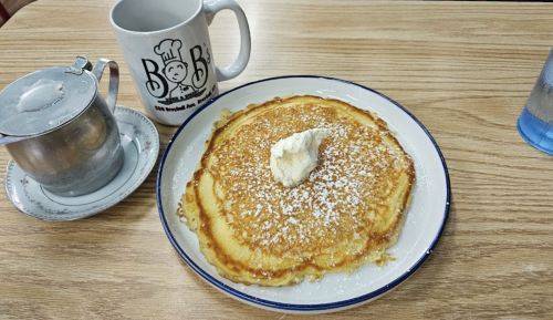 A plate of fluffy pancakes topped with butter and powdered sugar, alongside a coffee mug and a syrup container.