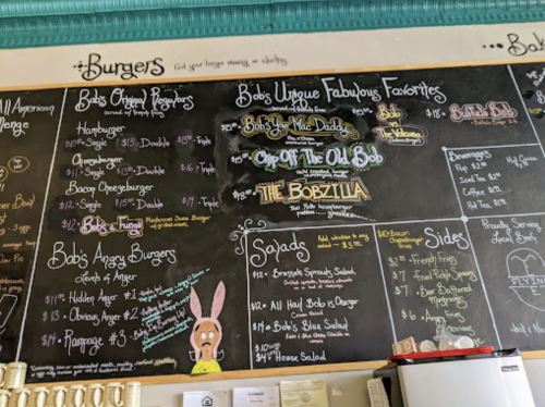 Chalkboard menu featuring burgers, salads, and sides with colorful handwritten descriptions and prices.