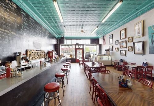 A cozy diner with red chairs, a long counter, and vintage decor, featuring a bright turquoise ceiling and large windows.