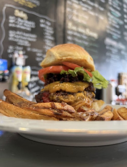 A juicy burger with lettuce, tomato, and melted cheese, served with golden fries on a white plate.