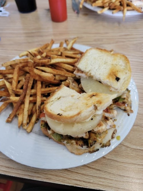 A plate with a grilled chicken sandwich on toasted bread and a side of crispy French fries.