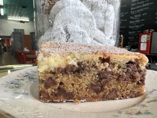 A slice of cake with a layered chocolate and cream filling, dusted with powdered sugar, on a decorative plate.
