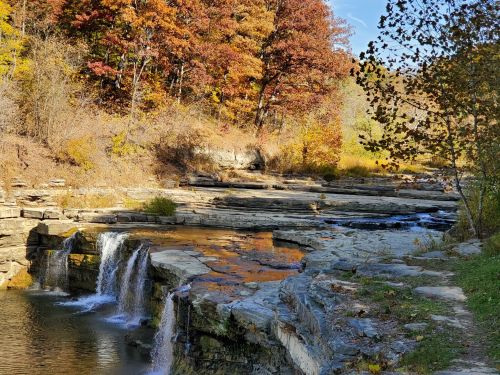 A serene landscape featuring a small waterfall surrounded by colorful autumn foliage and rocky terrain.