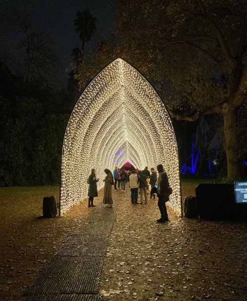 A glowing archway made of lights, with people walking through it in a dark, outdoor setting.