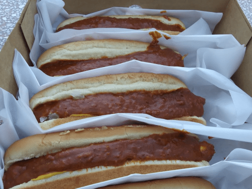 A box containing several hot dogs topped with chili, resting on white paper.