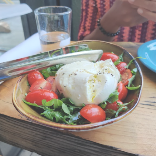 A bowl of fresh salad with cherry tomatoes and creamy burrata cheese, accompanied by a glass of water.