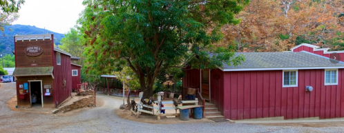 A rustic farm scene featuring red barns, a large tree, and gravel paths surrounded by greenery and hills.