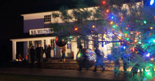 A decorated tree with colorful lights in the foreground, with people gathered outside a building at night.
