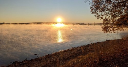 Sunrise over a misty river, with golden light reflecting on the water and trees lining the shore.