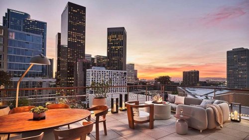 A stylish rooftop terrace with modern furniture, overlooking a city skyline at sunset.