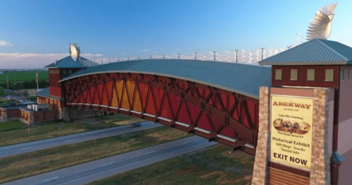 A colorful archway bridge with a sign for a historical exhibit, set against a clear sky and open landscape.