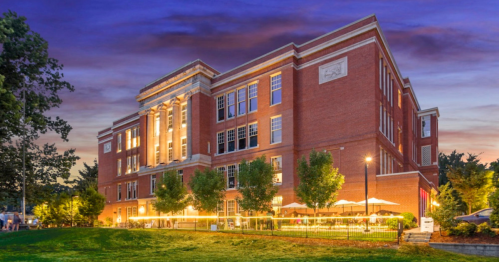 Historic brick building illuminated at dusk, surrounded by trees and outdoor seating.