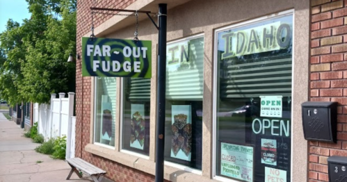 Sign for "Far-Out Fudge" outside a shop with large windows, showcasing various fudge displays.