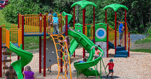 Children playing on a colorful playground with slides, climbing structures, and trees in the background.