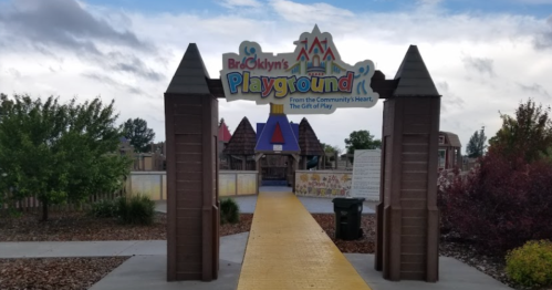 Entrance to Brooklyn's Playground, featuring a colorful sign and a yellow pathway surrounded by greenery.