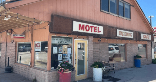 Exterior of a motel with a café, featuring a sign that reads "MOTEL" and "VACANCY," surrounded by potted plants.