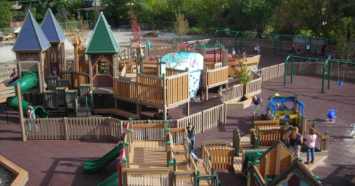 A colorful playground with slides, climbing structures, and children playing in a sunny outdoor setting.