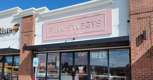 Exterior of a café named "Pink Sweets" with a pink sign, large windows, and an "OPEN" sign visible.