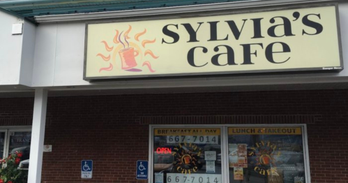 Sign for Sylvia's Cafe featuring a coffee cup graphic, with "Open" displayed in the window.