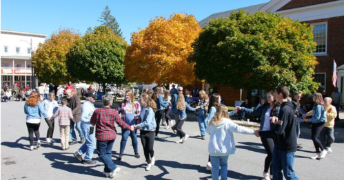 A lively outdoor dance scene with people in casual clothing, surrounded by colorful autumn trees.