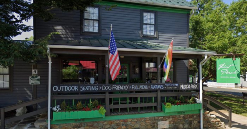 A charming gray building with outdoor seating, flags, and a sign promoting dog-friendly features and a full menu.