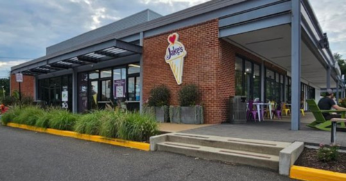 Exterior of Jake's ice cream shop, featuring a sign, large windows, and outdoor seating with greenery.