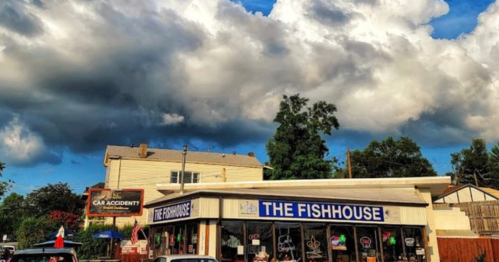 A restaurant called "The Fishhouse" under a dramatic sky with clouds, featuring a sign about a car accident nearby.