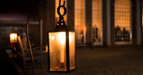 A glowing lantern hangs in the foreground, illuminating a dimly lit building with large windows in the background.