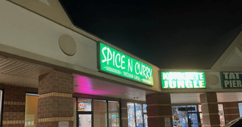 Neon signs for "Spice N Curry Indian Grill" and "Concrete Jungle" at night outside a shopping plaza.