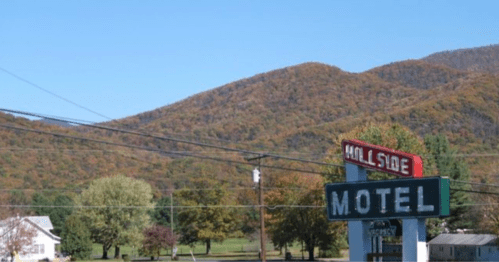 A motel sign in front of colorful, tree-covered mountains under a clear blue sky.