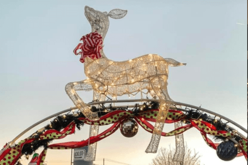 A lit reindeer decoration with a red bow, perched on an arch adorned with festive garlands and ornaments.