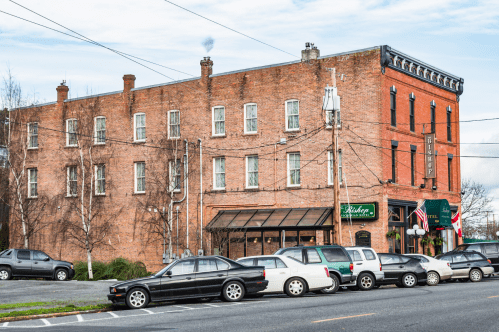 Historic brick building with multiple windows, featuring a restaurant and hotel sign, surrounded by parked cars.