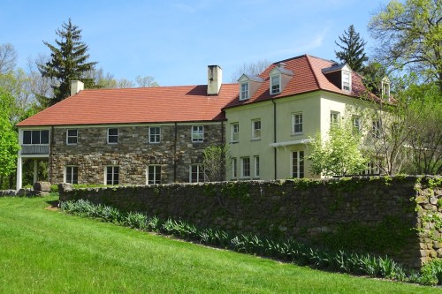 A large two-story house with a mix of stone and yellow siding, surrounded by green grass and trees.