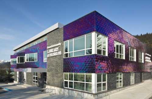 Modern building with colorful, reflective exterior, featuring large windows and surrounded by trees and mountains.