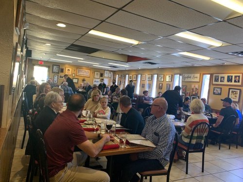A busy restaurant interior with diners at tables, chatting and enjoying meals in a lively atmosphere.