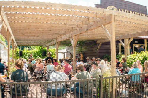 A lively outdoor gathering at a winery, with a crowd enjoying music under a wooden pergola.