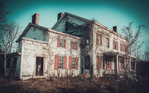 An abandoned, weathered house with overgrown vines and red shutters, set against a moody sky.