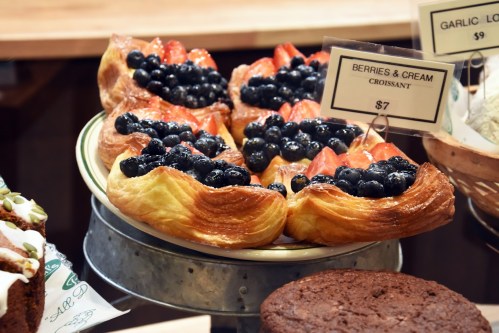 A display of croissants topped with strawberries and blueberries, labeled "Berries & Cream," priced at $7.