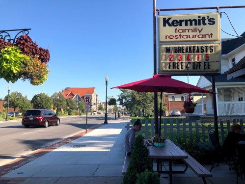 A street view of Kermit's Family Restaurant with a sign advertising breakfast specials and outdoor seating under an umbrella.