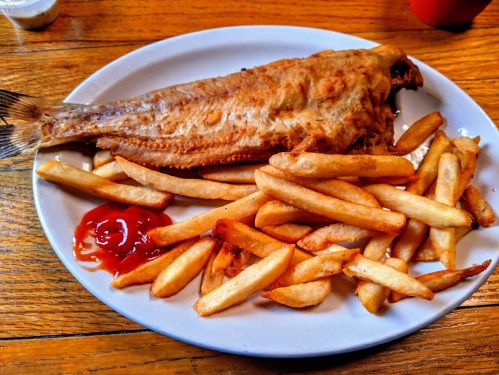 A plate of golden-brown fried fish served with crispy French fries and a side of ketchup.