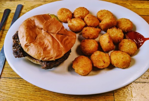 A plate with a hamburger and a side of golden, crispy tater tots with ketchup.