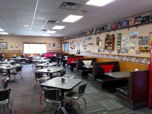 A cozy diner interior with booths and tables, decorated with vintage memorabilia on the walls.