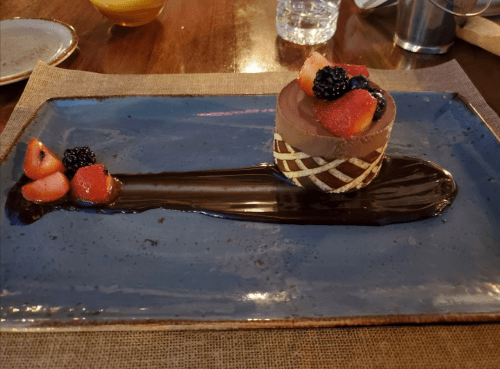 A chocolate dessert on a blue plate, garnished with strawberries and blackberries, with a chocolate sauce drizzle.