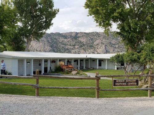 A white building with a sign reading "Mormon Handcart Visitors Center," surrounded by trees and mountains in the background.