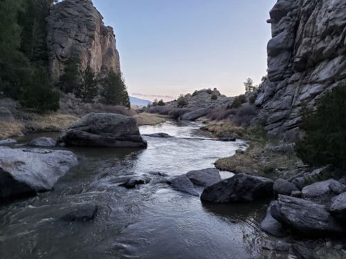 A serene river flows between rocky cliffs, surrounded by sparse vegetation under a twilight sky.